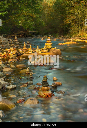Stacked rock cairns in tranquil river with golden light Stock Photo
