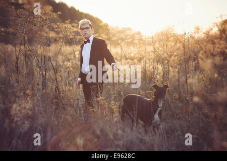 Young attractive man in suit and tie with a greyhound dog in autumn outdoors. He keeps the dog on the leash. Stock Photo