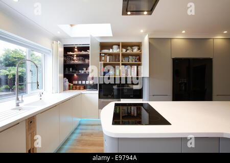 A modern white kitchen inside a home in the UK with cupboard doors open. Stock Photo