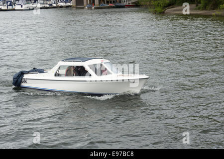 Four people in a self-drive hire motor boat on hire from Bowness bay Marina, near Bowness-on-Windermere on a dull and rainy day. Stock Photo