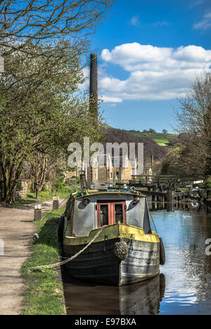 A narrow boat moored along the historic Rochdale canal near Todmorden  with old mill chimney in the background. Stock Photo
