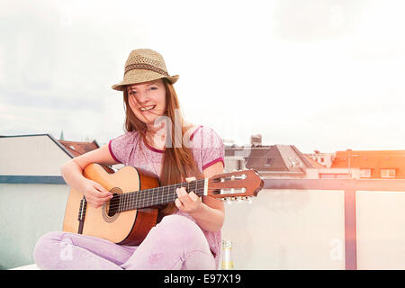 Young woman playing guitar on balcony, Munich, Bavaria, Germany Stock Photo