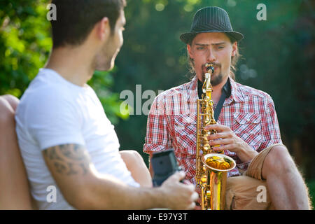 Young man playing saxophone, friend is listening Stock Photo