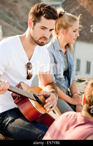 Young man playing guitar at rooftop party Stock Photo