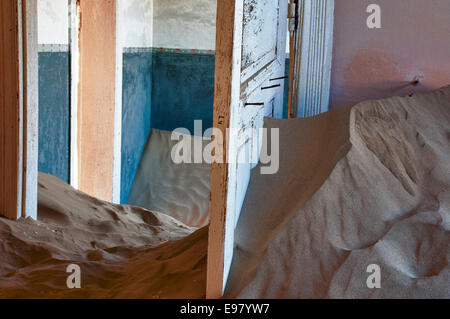 Open doors in a room full of sand in Kolmanskop, a ghost mining town in Namibia, Africa. The desert has reclaimed the town.