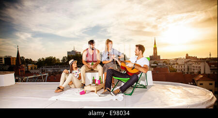 Young people listening to guitar music at rooftop party Stock Photo