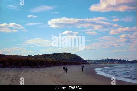 Figures in middle distance expanse beach by ocean dunes in background golden overhanging clouds; magical evening colors. Stock Photo