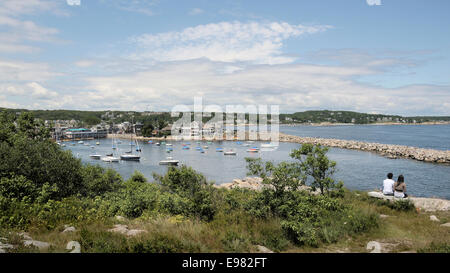 A young couple sitting on hillside are looking downward at Rockport Bay filled various size recreational craft long stone Stock Photo
