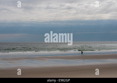 Sole figure on broad vista beach surf ocean sky. Solitude self refection are theme. Light is spiritual cloud formations Stock Photo
