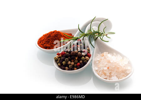 Himalayan rock salt, red cayenne pepper and black peppercorns in ceramic spoons with a sprig of fresh rosemary for seasoning and flavouring food Stock Photo