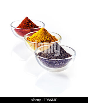 Three clear glass bowls of colourful of ground spice and black lava salt in conical heaps arranged in a receding row on a white Stock Photo