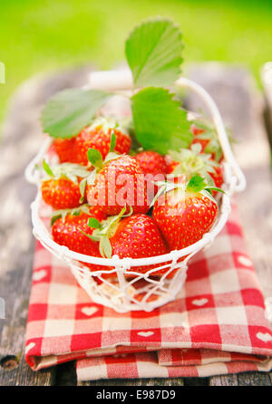 Fresh strawberries in small white basket on wooden table in nature - picnic meal Stock Photo