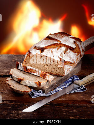 Sliced fresh rye bread on a rustic wooden table in front of a roaring fire Stock Photo