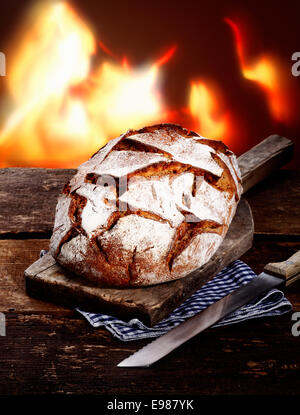 Rye bread on a rustic wooden cutting board on an old country table in front of the fire Stock Photo