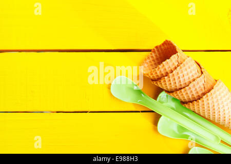 Ice cream cones and green plastic spoons on yellow table with copy space Stock Photo