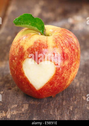 Ripe red apple with a heart shape neatly cut of the skin on a textured weathered wooden surface Stock Photo