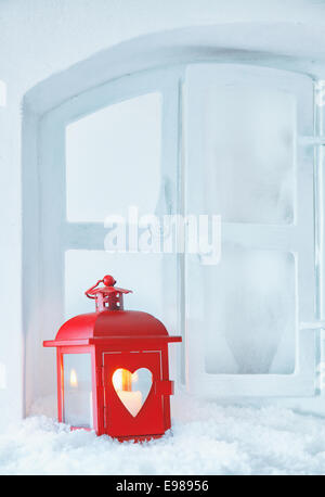 Cheerful red Christmas lantern with a glowing candle standing on a snowy windowsill with copyspace for seasonal greetings Stock Photo