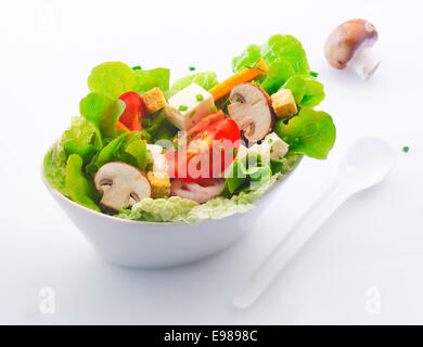 Individual side serving in a white china dish of fresh mixed green salad with sliced fresh mushrooms , tomato and feta cheese