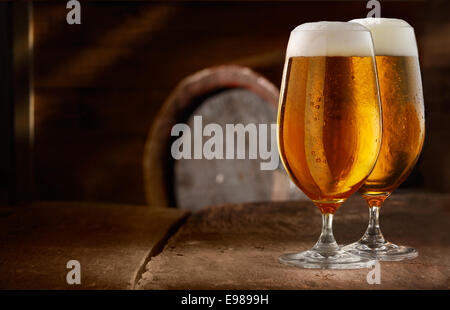 Two glasses of fresh foamy beer on a table in a vintage beer cellar with a barrel in the background Stock Photo