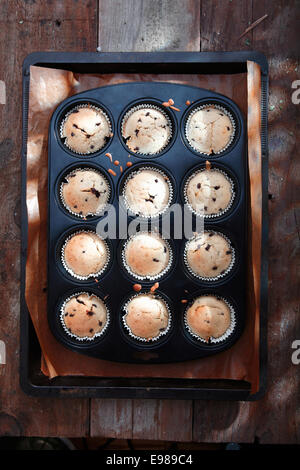 Overhead view of a baking tray with freshly baked muffins from the oven cooling on an old wooden surface Stock Photo