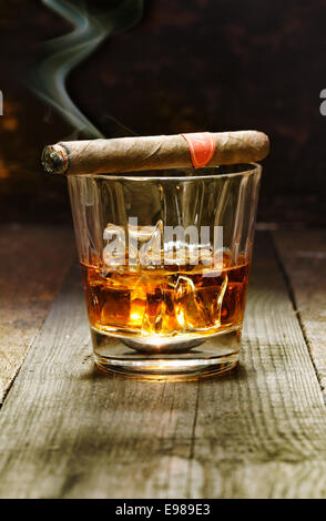 Burning Cuban cigar resting on a glass of brandy in a bar, the luxury pleasures of a wealthy macho man Stock Photo