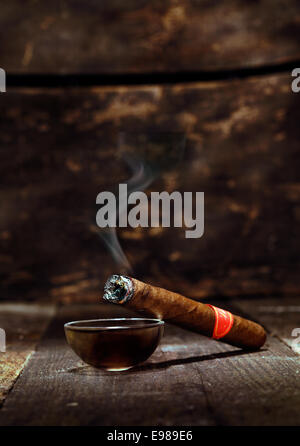 Burning handmade luxury Cuban cigar resting on an ashtray on an old wooden countertop in a nightclub or bar with copyspace Stock Photo