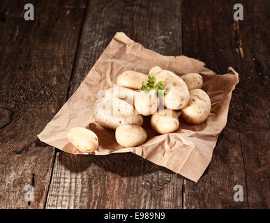 Fresh washed farm potatoes displayed on crumpled brown paper on a wooden tabletop Stock Photo