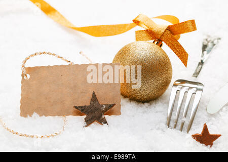 Festive place setting with Christmas decorations and silver cutlery in fresh winter snow with a decorative blank gift tag Stock Photo