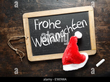 Frohe Weihnachten Christmas greeting handwritten in German on a chalkboard slate with a colourful red Santa hat Stock Photo