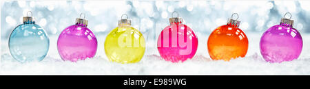 Colourful translucent Christmas baubles arranged in a row in snow against sparkling party ligts suitable as a banner or border Stock Photo