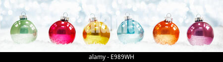 Beautiful shiny Christmas ball banner arranged in a row on fresh white winter snow with a backdrop of sparkling lights Stock Photo