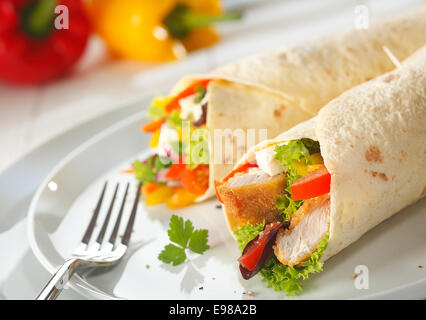 Delicious rolled golden wrap with a filling of fresh salad ingredients, feta cheese and chunks of crisp crunchy chicken wings served on a plate Stock Photo