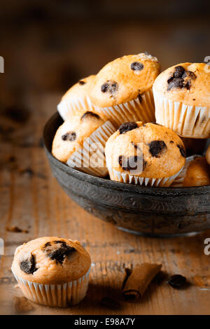 A single mini muffin on aged wooden table, with a further bowl of muffins in the background Stock Photo