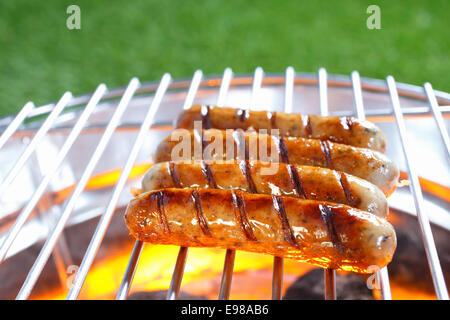 Row of beef and pork sausages sizzling on a hot barbecue over glowing coals while being cooked on a healthy outdoor barbecue Stock Photo