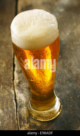 High angle view of a tall glass of chilled beer with a frothy head standing on an old grunge wooden table Stock Photo