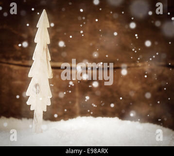 Pretty Christmas card background with a simple wooden Christmas tree standing in snow during a snowfall against a rustuc wooden Stock Photo