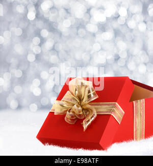 Colourful red Christmas gift decorated with a gold ribbon and bow in winter snow with a bokeh of falling snowflakes and copyspace for your seasonal greeting Stock Photo