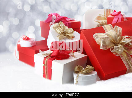 Pretty Christmas gifts and boxes with decorative bows and ribbons in red, white and gold, on a bed of white winter snow Stock Photo