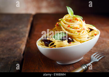 Spaghetti pasta in a white bowl with olives on a dark wooden table. Stock Photo
