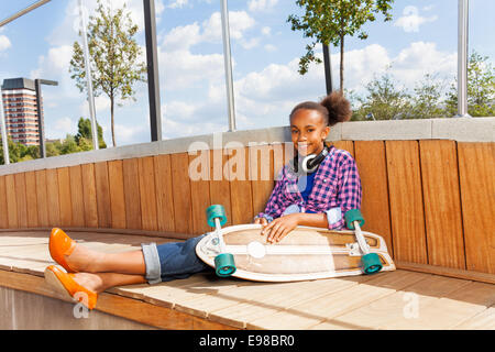 Girl with skateboard sits on wooden construction Stock Photo
