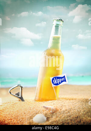Capped bottle of chilled fruity orange soda or ale (beer) standing in the golden sand on a tropical beach with a bottle opener and Skipper sign. Look at my portfolio for more cocktails. Stock Photo