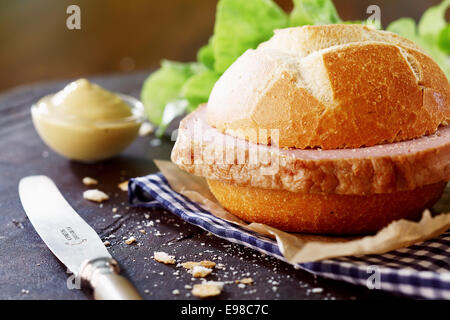 Preparing a traditional German meat loaf roll in a rustic kitchen with a hearty slice of meat on a crusty white freshly baked bun Stock Photo