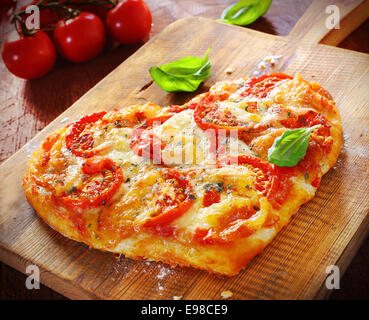 Heart shaped vegetarian pizza topped with cheese and tomato on an old wooden board signifying love of pizza, or romantic love for Valentines day or an anniversary