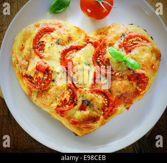 Overhead view of a romantic heart shaped Italian pizza topped with a vegetarian topping of golden melted cheese and tomato on a