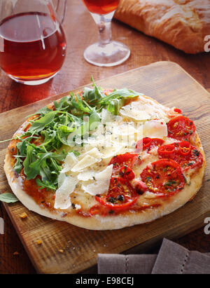 Italian pizza in the red, white and green colours of the national flag formed by the three toppings of tomatoes, cheese shavings and fresh rocket leaves on a wooden board served with a light red wine Stock Photo