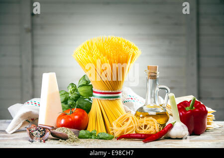 Uncooked Italian spaghetti tied with a ribbon in the colours of the national flag arranged on a counter with cheese, tomato, basil, chilli pepper, garlic, olive oil and sweet pepper Stock Photo