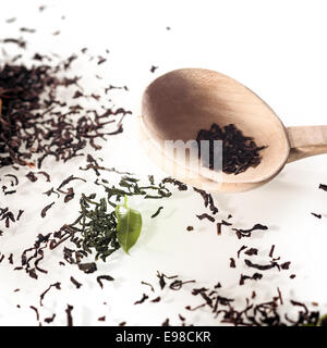 Dried loose shredded tea leaves scattered on a white surface with a fresh green leaf and rustic handcrafted wooden spoon Stock Photo