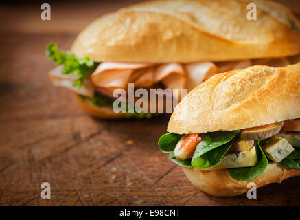 Two delicious savory rolls for a lunchtime snack on an old rustic wooden table with focus to the roll filled with cheese, fresh Stock Photo