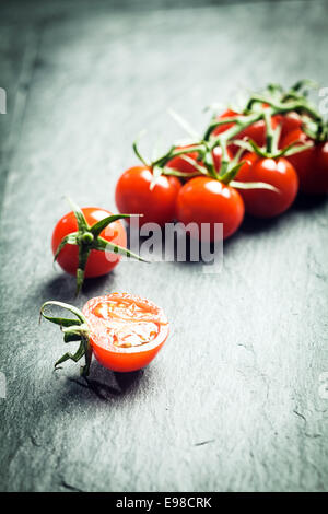 Grape tomatoes on the vine with a single halved tomato in the foreground on a textured surface with highlight and copyspace and Stock Photo