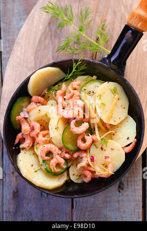 Delicious gourmet meal of prawns pan fried with potato and zucchini garnished with herbs and served in a metal skillet Stock Photo
